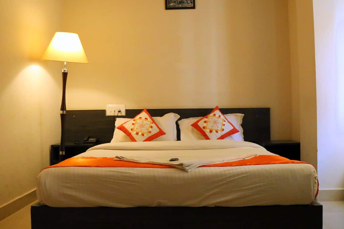 Una cama bien tendida con ropa blanca y detalles naranja, una lámpara de noche y un pequeño cuadro en la pared.