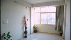 Quarto com uma janela grande, um vaso de planta e um interruptor de luz fixado na parede.