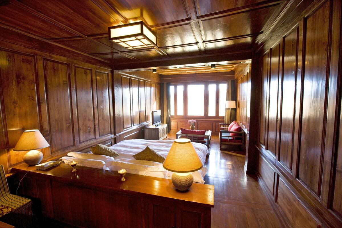 Una habitación con paneles de madera, una cama, lámparas de noche, un escritorio y un ventanal con luz natural.