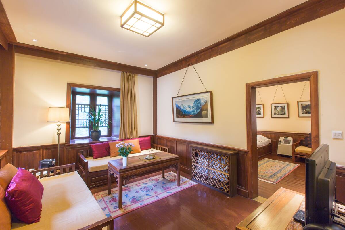 Una habitación acogedora con un banco de madera, una mesita, un televisor y un ventanal con cortinas.