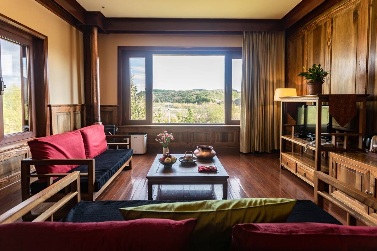 Una habitación acogedora con un sofá de madera, una mesita con un florero y un televisor sobre un mueble de madera.