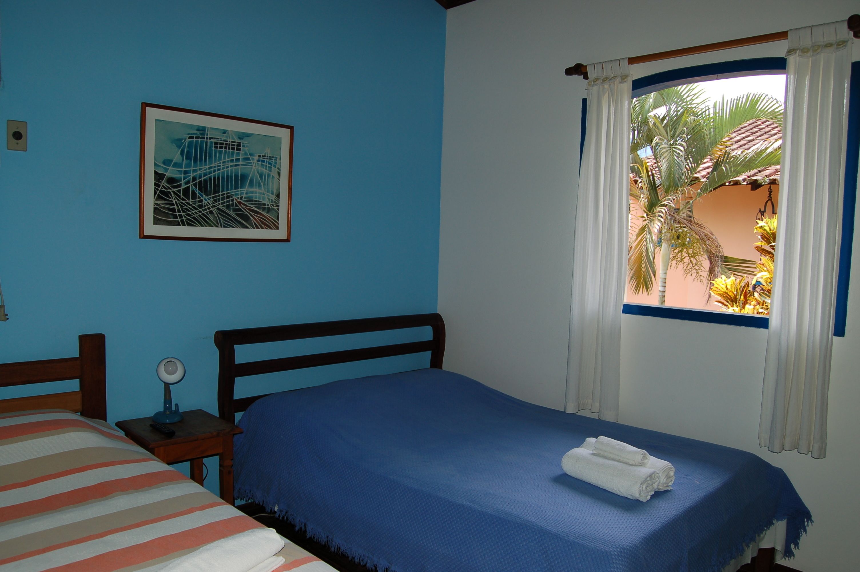 A bedroom with a single bed, a bedside table with a lamp, a framed picture on the wall, and a window with curtains.