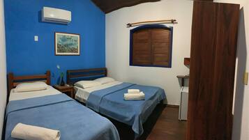 A room with two beds, a wooden door, a small table, and a window with a wooden frame.