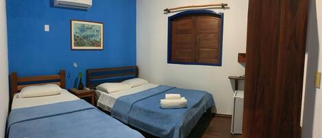 Una habitación con dos camas, una puerta de madera, una mesita pequeña y una ventana con marco de madera.