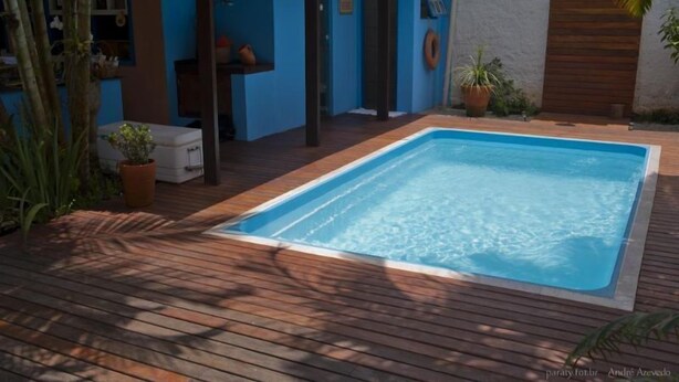 A rectangular swimming pool with a wooden deck surrounding it. - Pousada Manacá (Paraty)
