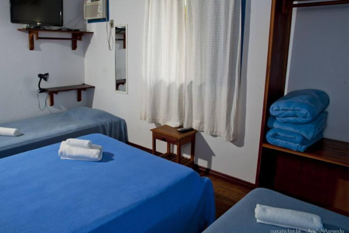 A hotel room with two beds, a TV, a mirror, a small table, and a shelf with towels.