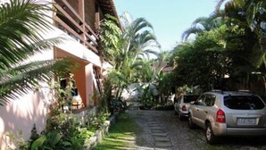 A residential area with a paved driveway, parked cars, and lush greenery including palm trees. - Pousada Manacá (Paraty)