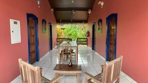 A covered dining area with a table and chairs, a view of greenery outside, and a fire extinguisher on the wall. - Pousada Manacá (Paraty)