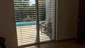 A room with a wooden floor, a bed, a chair, and a view of a pool through a sliding glass door. - villa near Ajaccio with swimming pool in the heart of nature (Ocana)