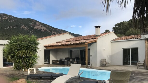A pool area with lounge chairs, a wooden deck, and a mountain backdrop. - villa near Ajaccio with swimming pool in the heart of nature (Ocana)
