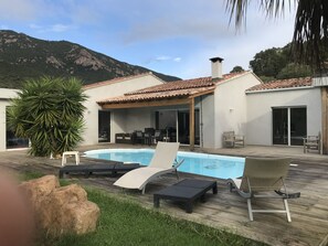 Zona piscina con lettini, un pontile in legno e uno sfondo montuoso.