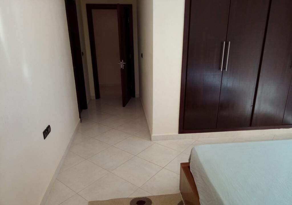 A bedroom with a bed, a wardrobe, and a hallway leading to another room.
