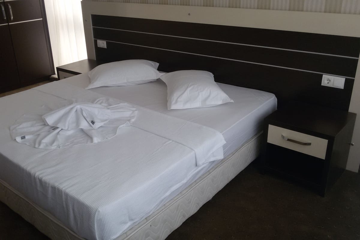 Una cama bien hecha con sábanas blancas, un cabecero y una mesita de noche con un cajón.