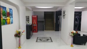 Un vestíbulo moderno con un refrigerador de Coca-Cola, un mostrador de recepción y una escalera que sube a los pisos superiores.