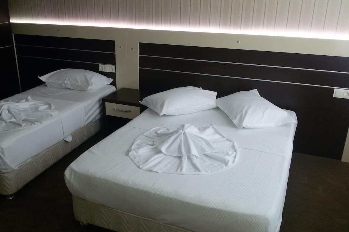 Dos camas individuales con sábanas y almohadas blancas, una mesita de noche y un aplique de pared.