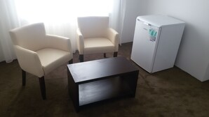 Una habitación con dos sillones blancos, un refrigerador pequeño blanco y una mesa de centro de madera oscura.