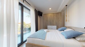 A modern bedroom with a large bed, a wooden wardrobe, a TV mounted on the wall, and a view of the outside through a large window. - Istrian Pearl (Rasa)