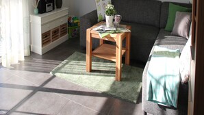 Un salon avec un canapé gris, une table basse en bois, un meuble de télévision blanc et un téléviseur fixé au mur.