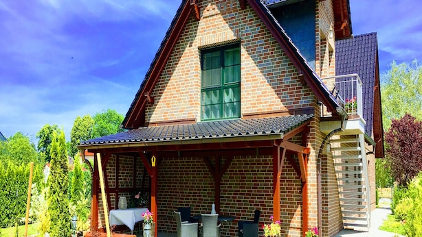 Une maison à deux étages avec une façade en briques, un porche couvert et un petit balcon.