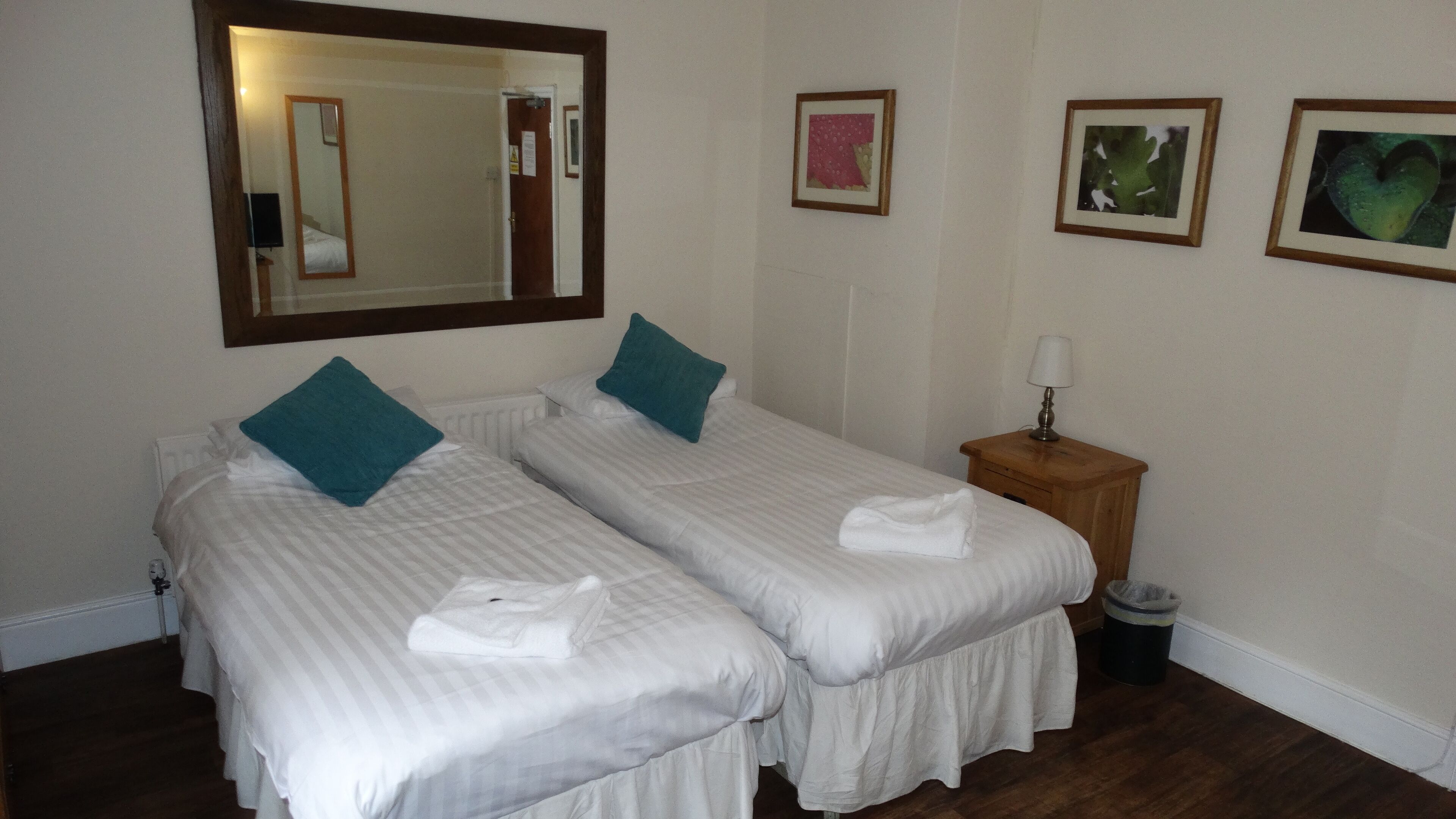 A hotel room with two single beds, a wooden nightstand with a lamp, and a mirror on the wall.