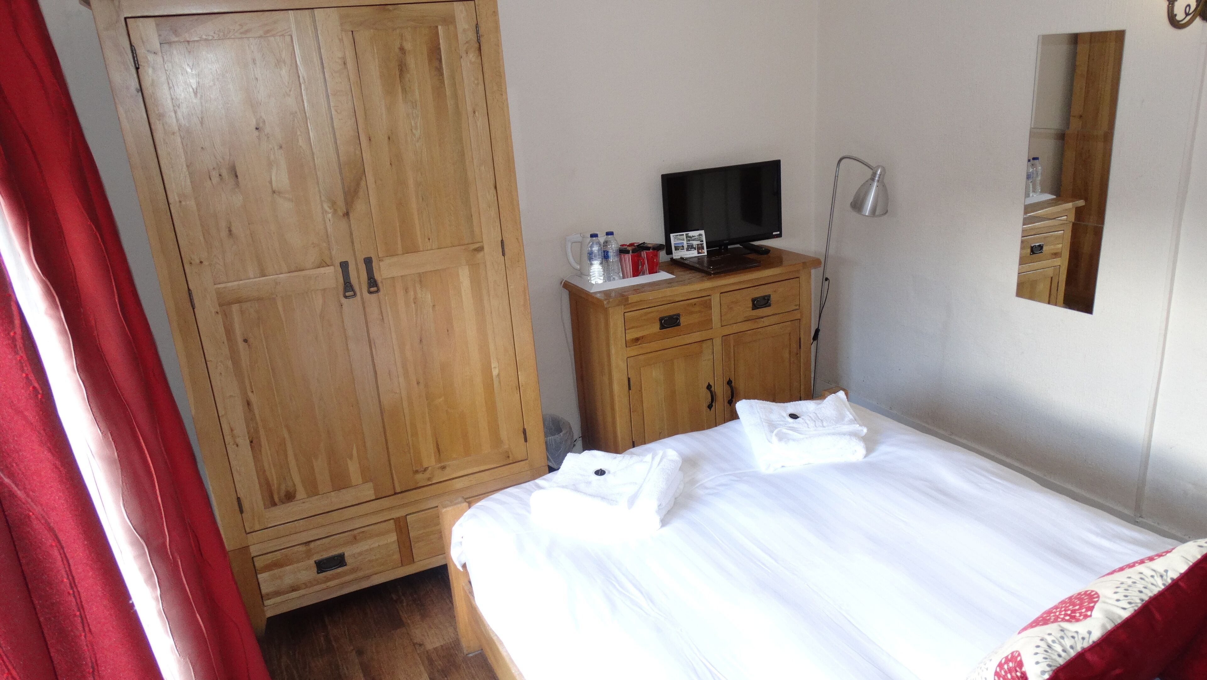 A bedroom with a wooden wardrobe, a television on a wooden cabinet, and a bed with white bedding.
