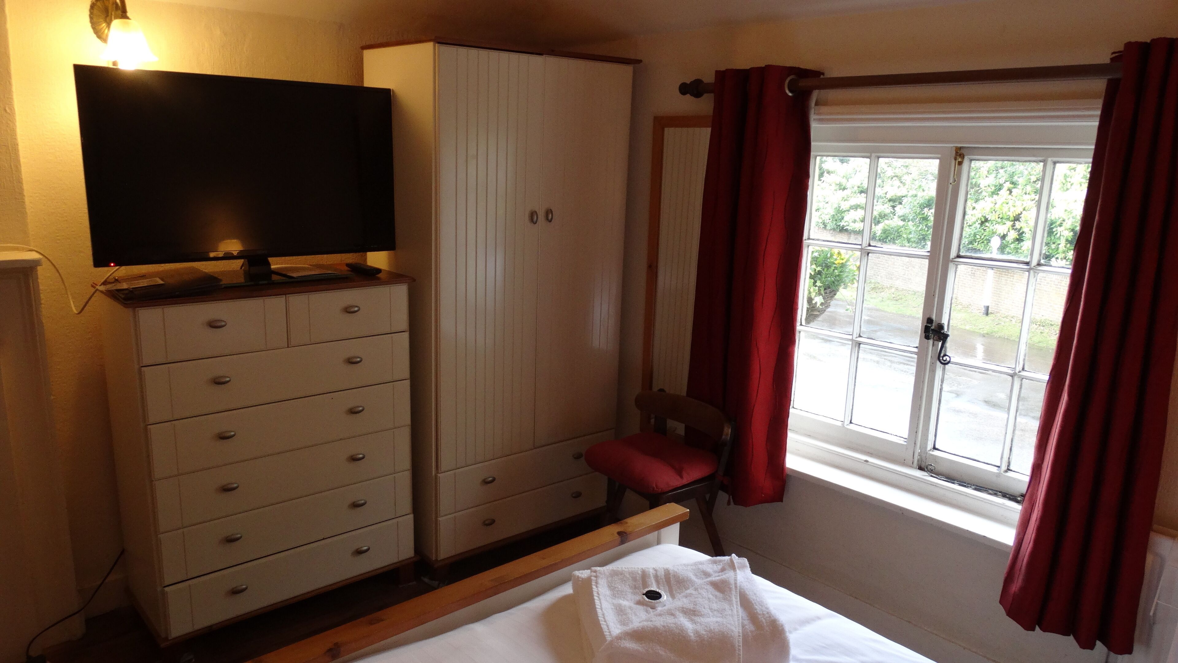 Un dormitorio con una cama, un aparador, un televisor y una ventana con cortinas.