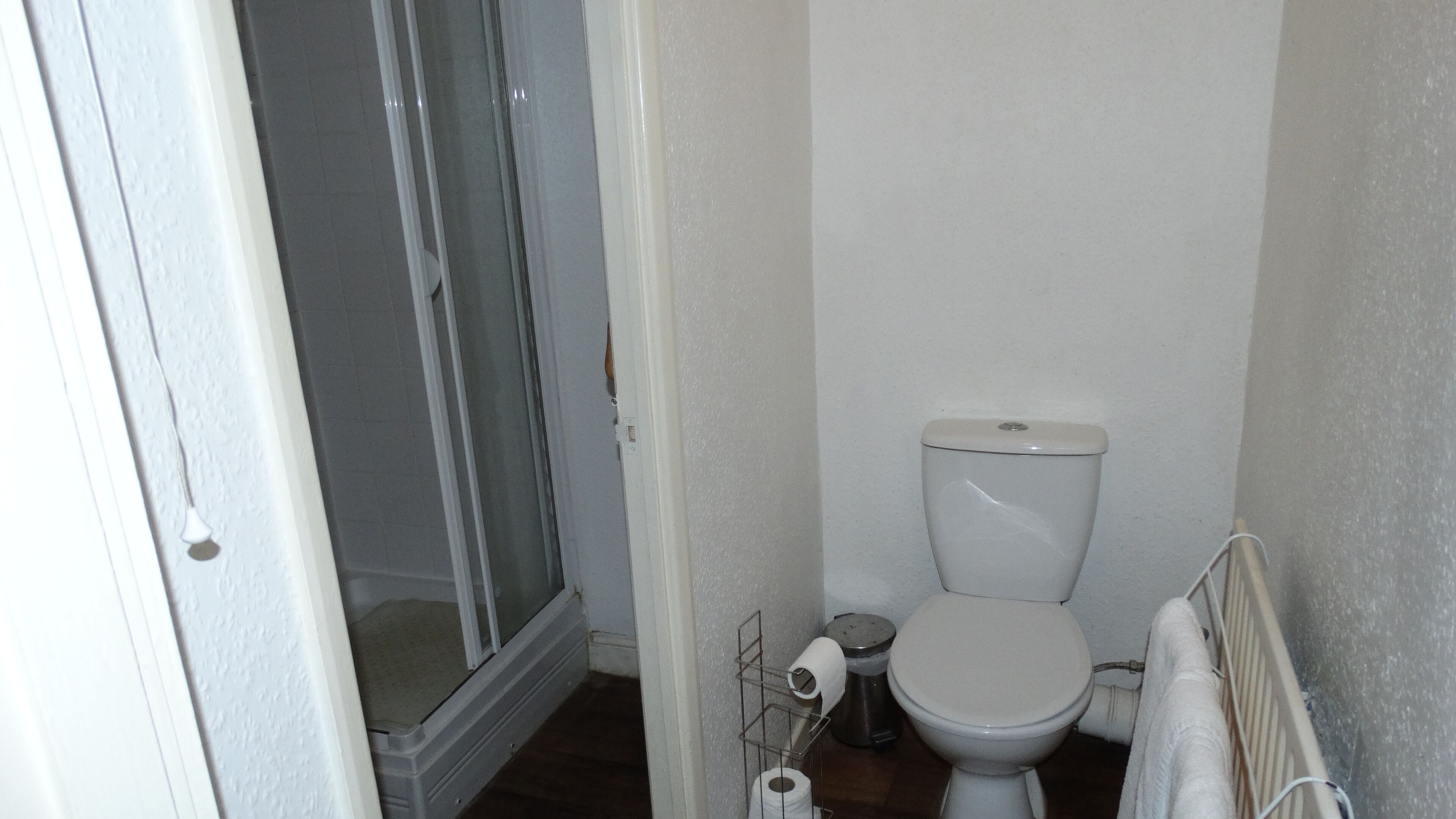 Pieni kylpyhuone, jossa on wc, suihku ja wc-paperiteline.