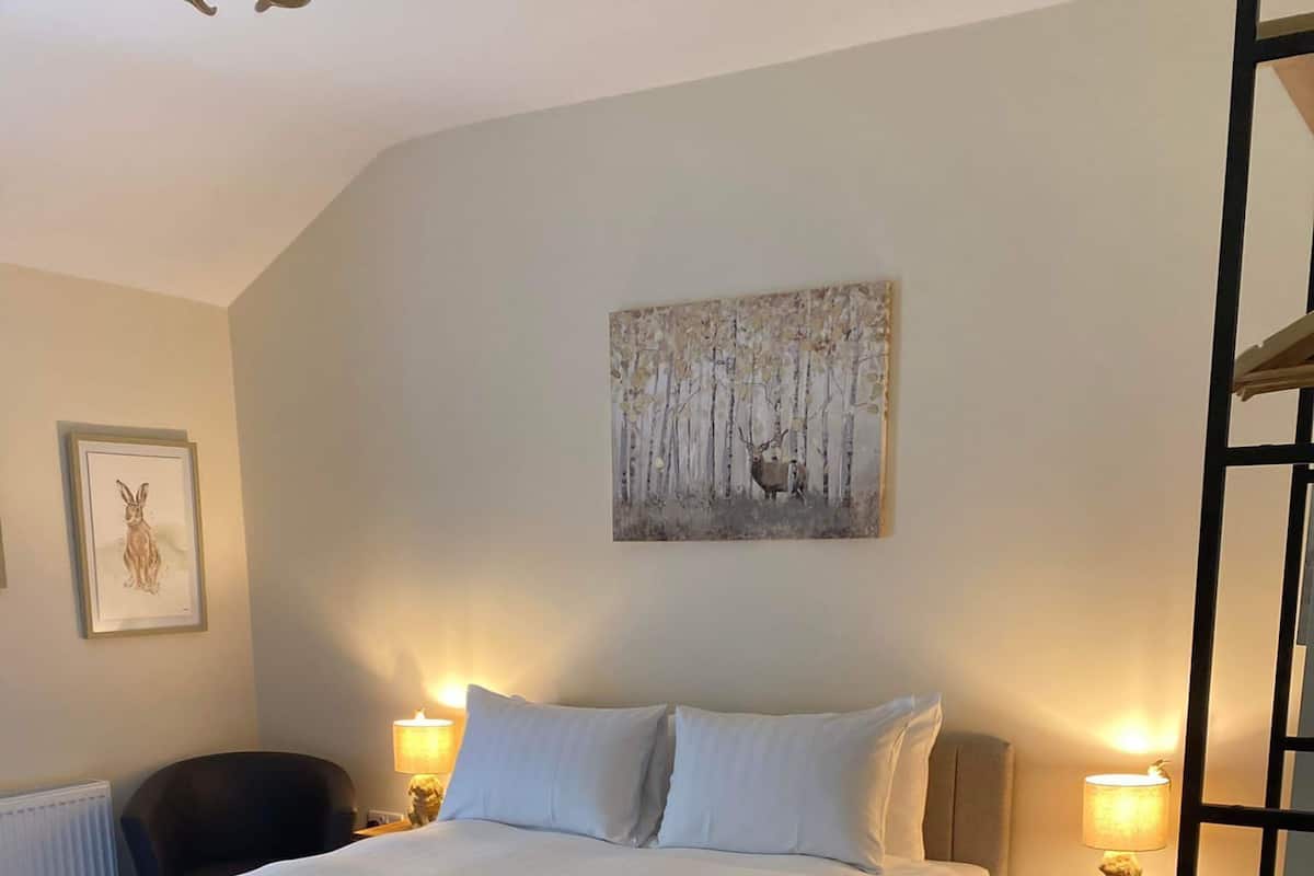 A bedroom with a large bed, two bedside tables, a chair, a radiator, and a painting on the wall.