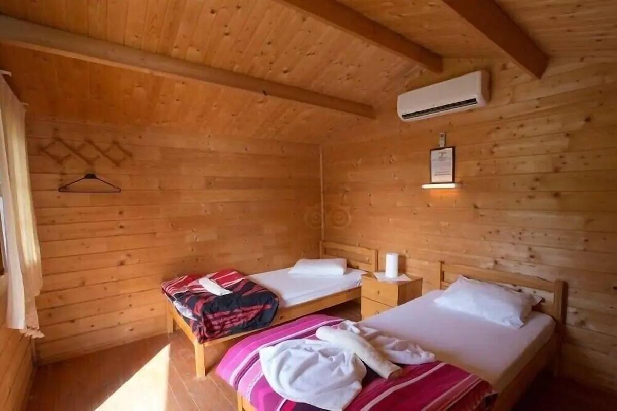 Une chambre dans un chalet en bois, avec deux lits, un porte-manteau suspendu et un appareil de climatisation.
