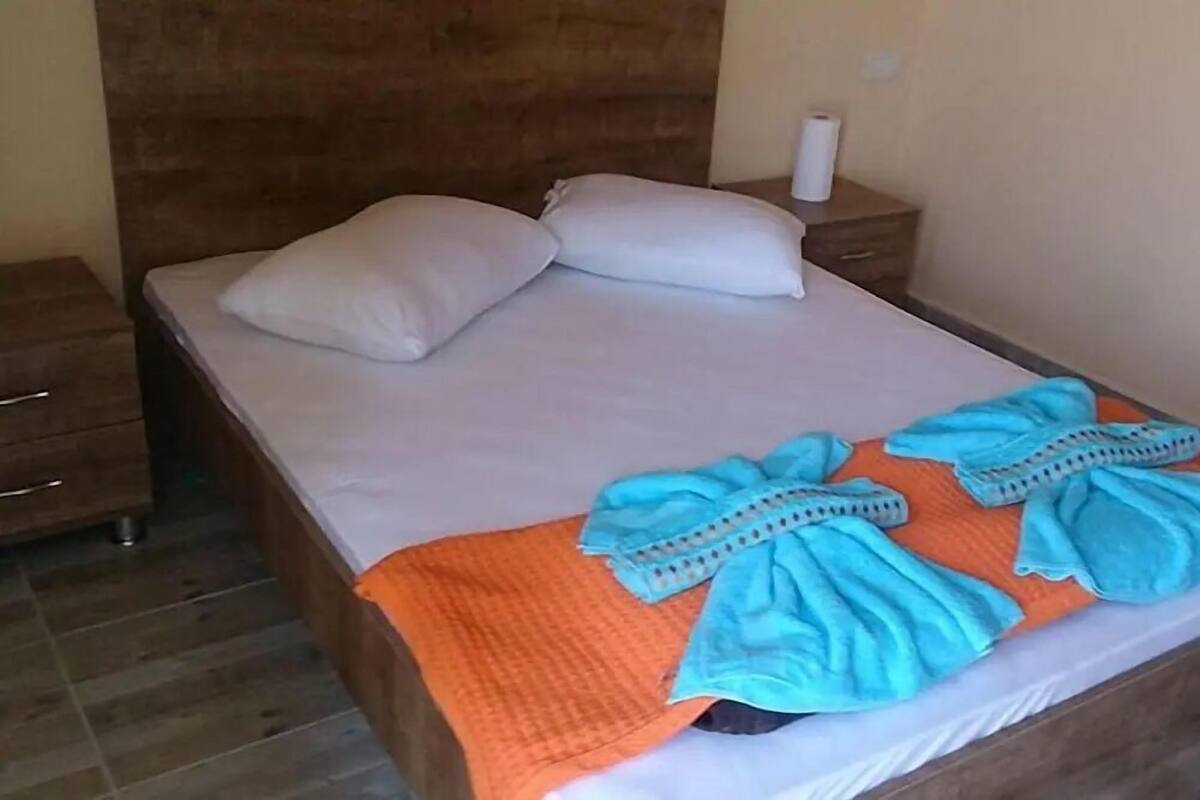 Un lit bien fait, avec des oreillers blancs, une couverture orange et des serviettes bleues.