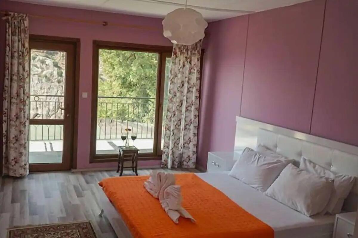 Une chambre avec un lit, une table de chevet, une fenêtre avec des rideaux et un balcon donnant sur une vue agréable.