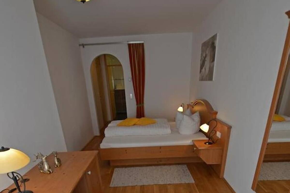 Une chambre à coucher de taille modeste, comprenant un lit simple, une table de chevet, une lampe et un petit tabouret.