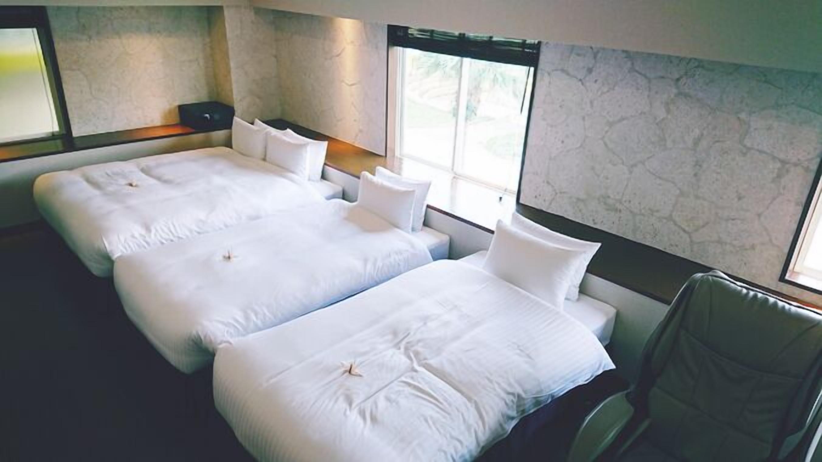 Habitación de hotel con dos camas, una silla y un amplio ventanal.