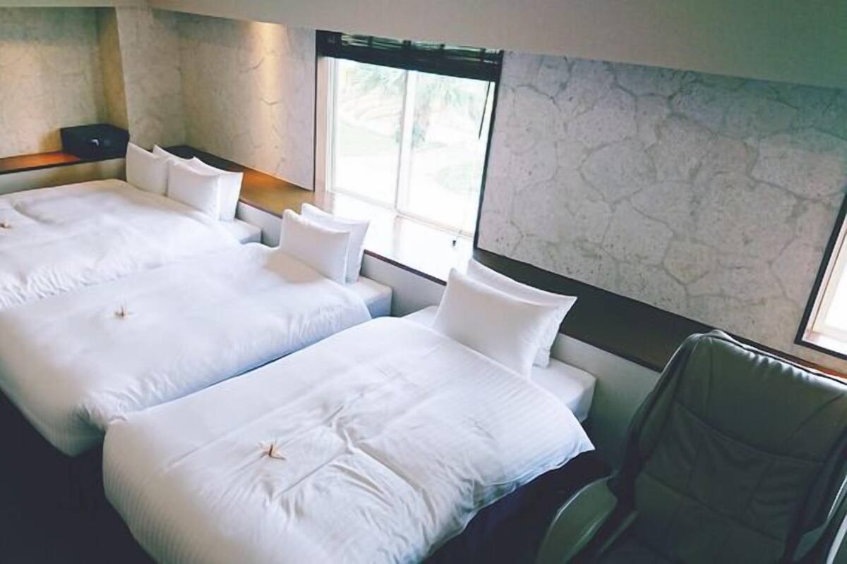 A hotel room with two beds, a chair, and a large window.