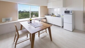 A modern kitchen with white cabinets, a microwave, and a dining area with a wooden table and chairs. - Wires Hotel (Naha)