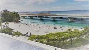 A beach with a bridge, clear water, and people sunbathing. - Wires Hotel (Naha)