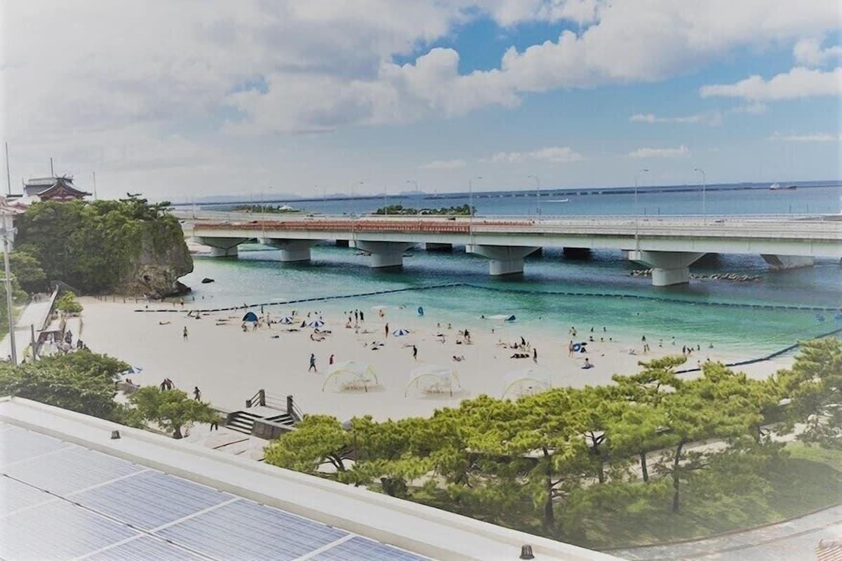 A beach with a bridge, clear water, and people sunbathing.