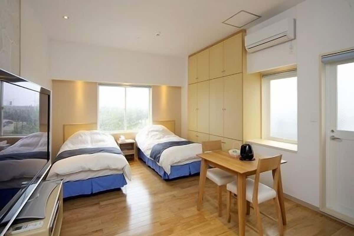 A hotel room with two beds, a wooden desk, a chair, and a TV.