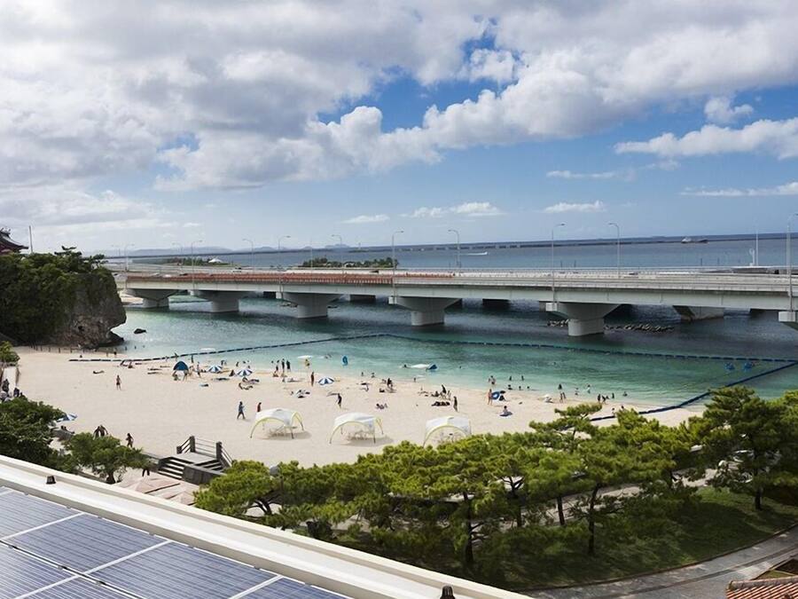 A beach with a bridge overhead, clear water, and a view of the sea.