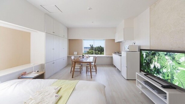 A modern hotel room with a bed, a dining table with chairs, a kitchen area, and a television. - Wires Hotel (Naha)