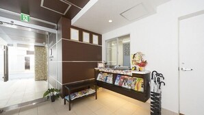 A reception area with a glass door, a reception desk with magazines, a plant, and an umbrella stand. - Wires Hotel (Naha)