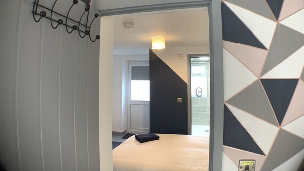 Ein Hotelzimmer mit Wandpaneelen mit geometrischem Muster, einem Bett mit weißer Bettdecke, einem schwarzen Kopfkissen und einer Wandleuchte.
