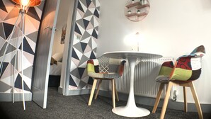 Ein modernes Zimmer mit Wand im geometrischen Muster, einem runden Tisch mit Stühlen, einer Stehlampe und einer Heizung.