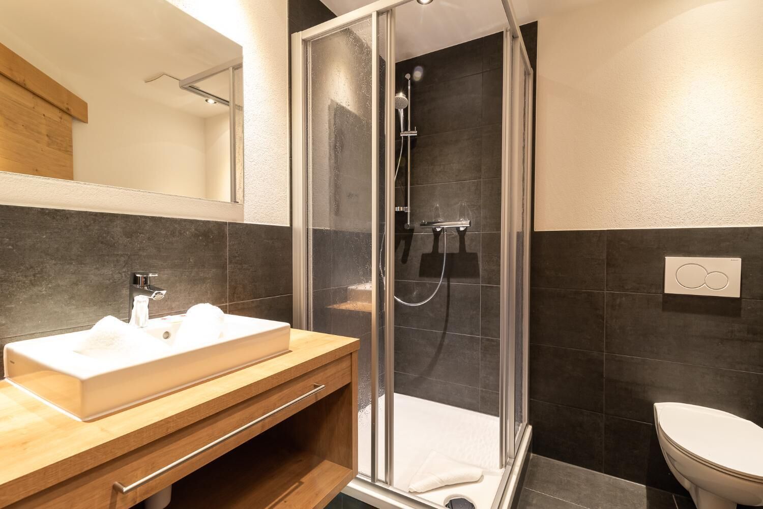 A modern bathroom with a glass-enclosed shower, a wooden vanity with a white sink, and a white toilet.
