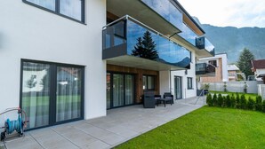 A modern two-story house with large glass windows, a covered patio with outdoor furniture, and a well-maintained lawn. - A CASA Elegance (Laengenfeld)