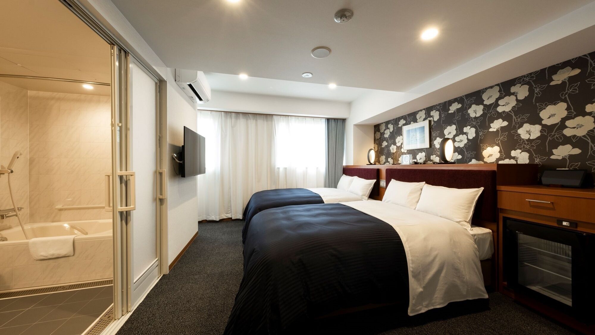 Habitación de hotel con ducha, dos camas, televisión y papel tapiz floral.