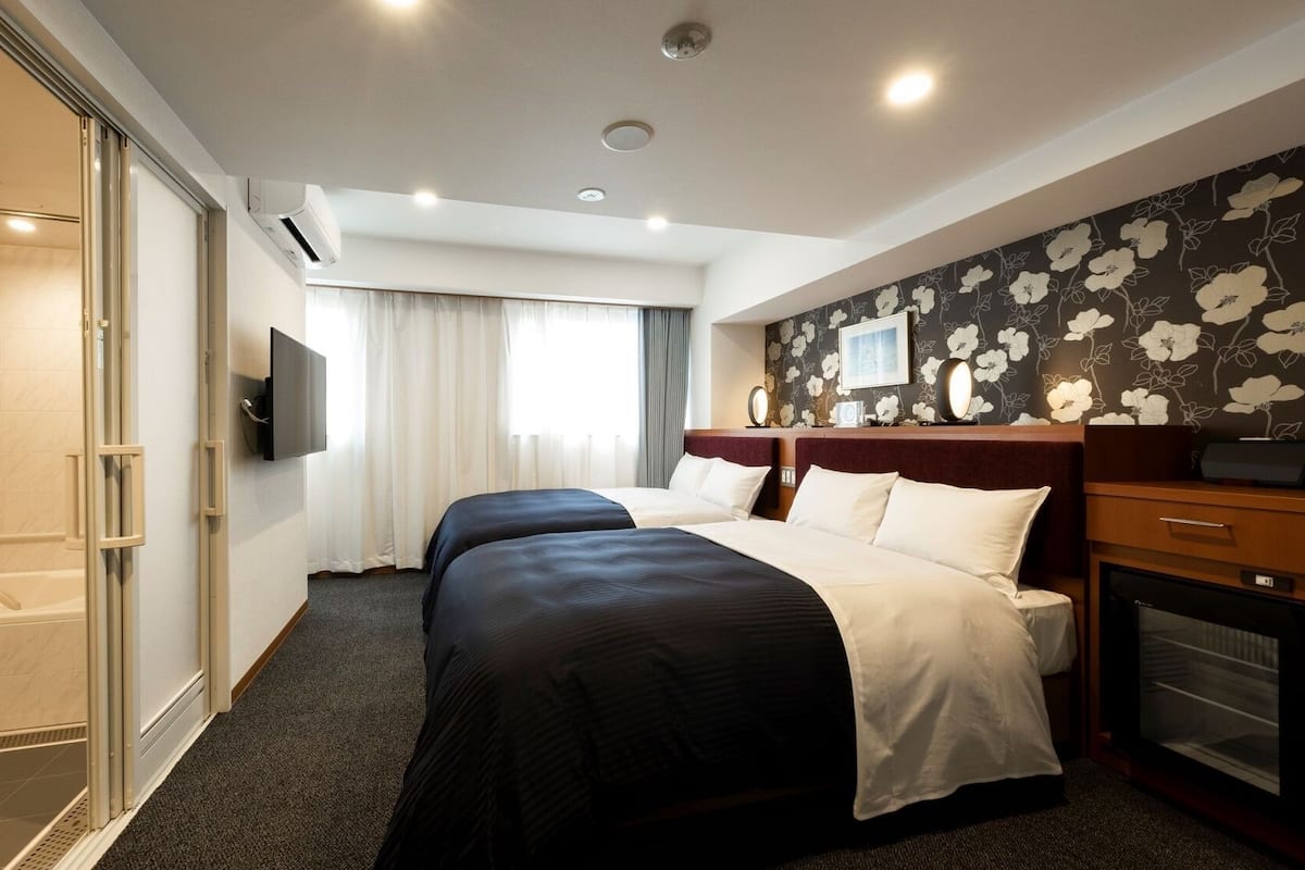 Habitación de hotel con ducha, dos camas, televisión y papel tapiz floral.