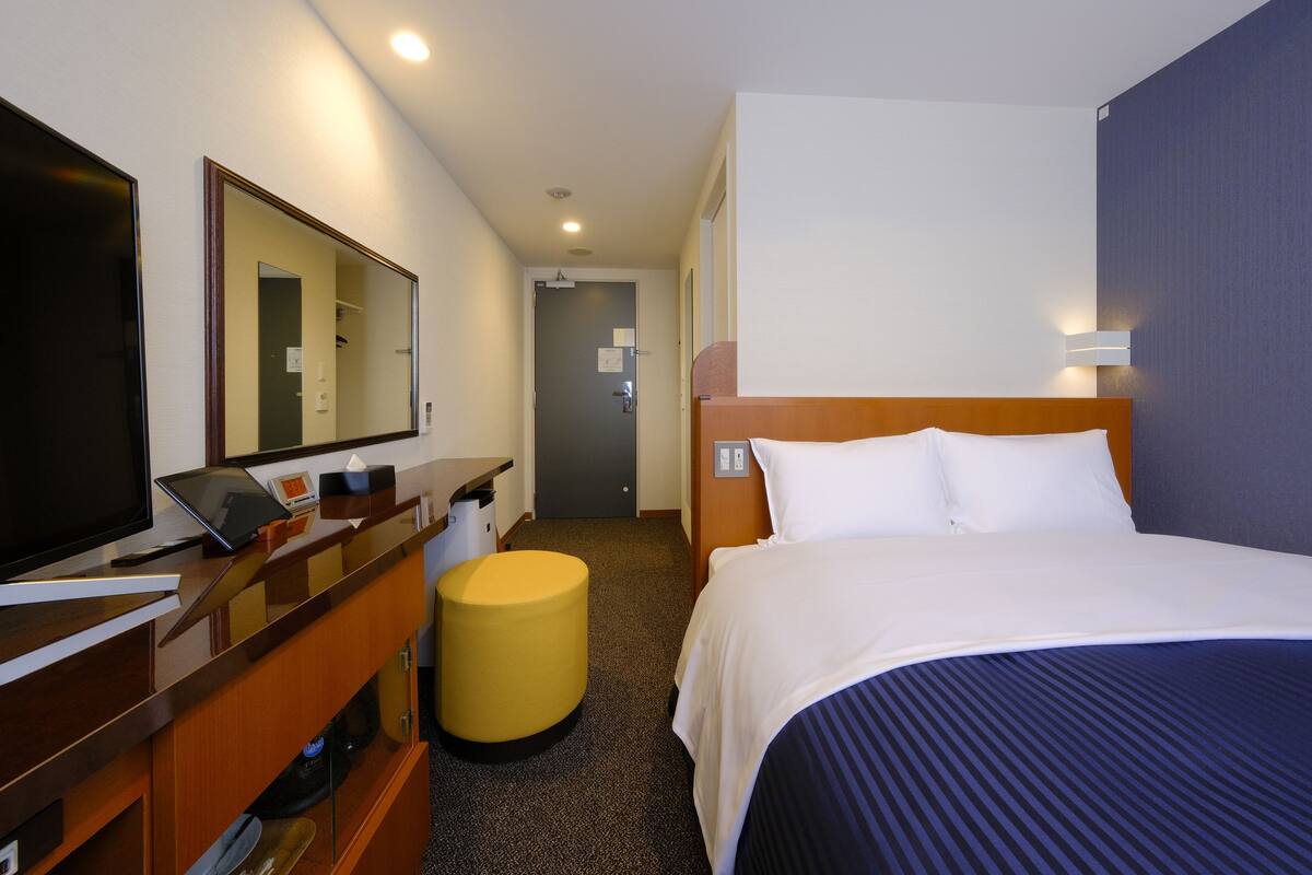 Ein Hotelzimmer mit einem Bett, einem Schreibtisch mit Computer, einem Spiegel und einem kleinen Hocker.