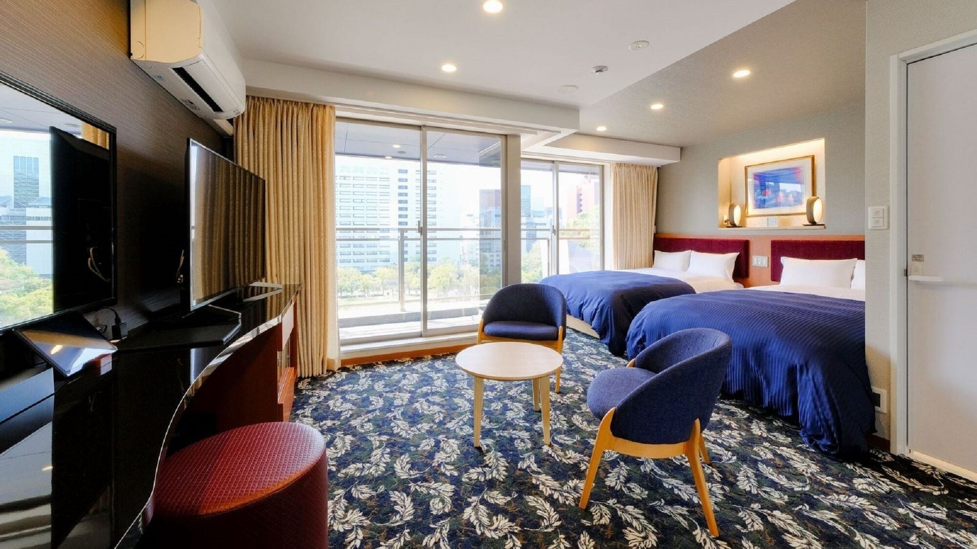 A hotel room with two beds, a TV, a desk, a chair, and a large window with a city view.
