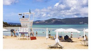 Un poste de surveillance des sauveteurs se dresse sur une plage, avec un ciel dégagé et des montagnes en arrière-plan.